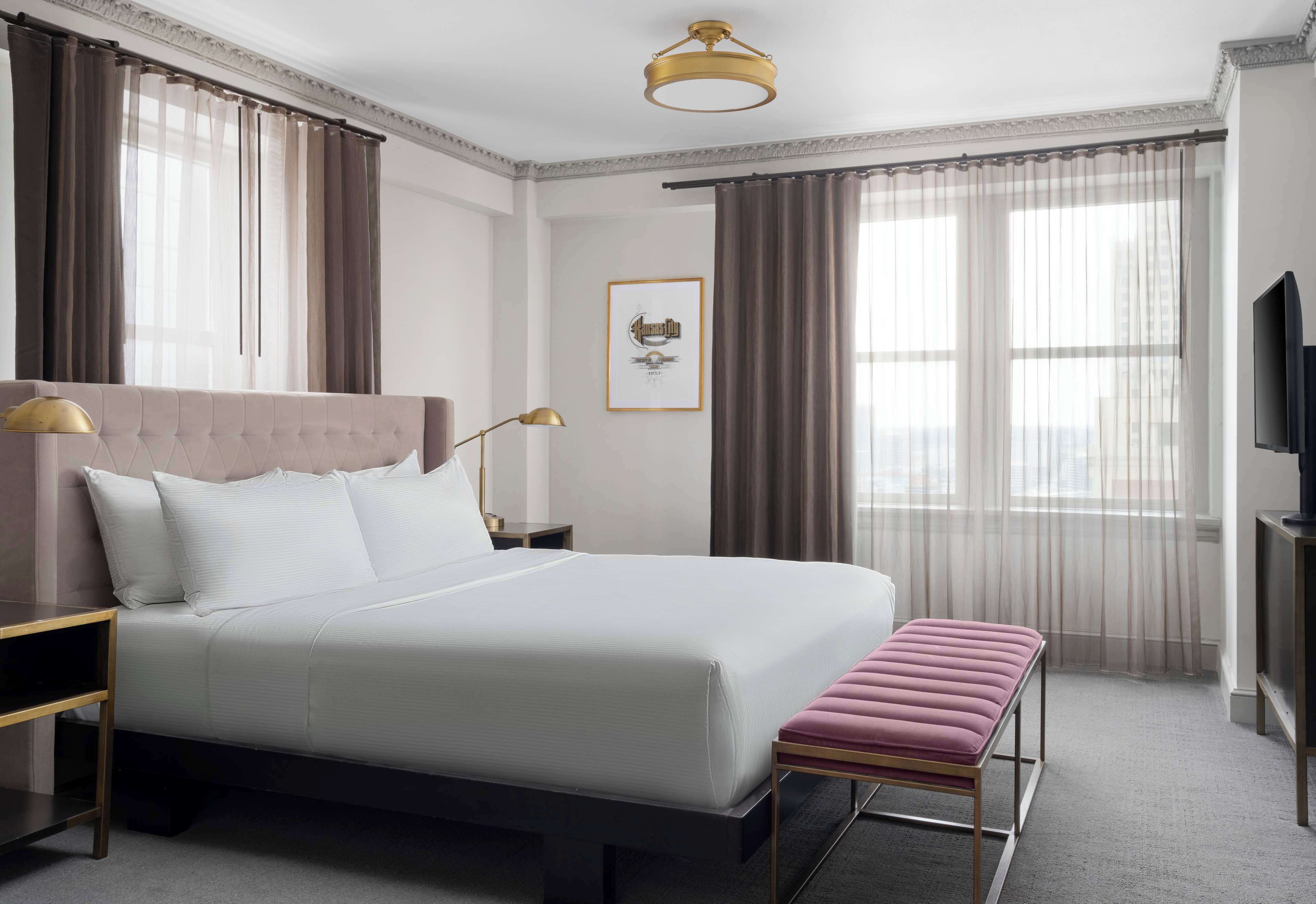 A hotel room with a large bed, a bench, a TV, and a framed picture on the wall.