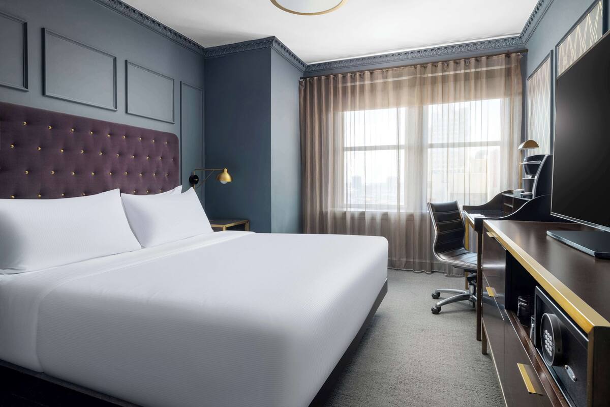 A hotel room with a large bed, a desk with a computer, a chair, and a TV.