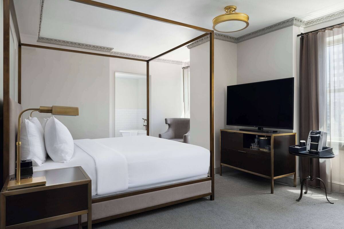 A four-poster bed with a television and coffee maker on a wooden console table beside it.