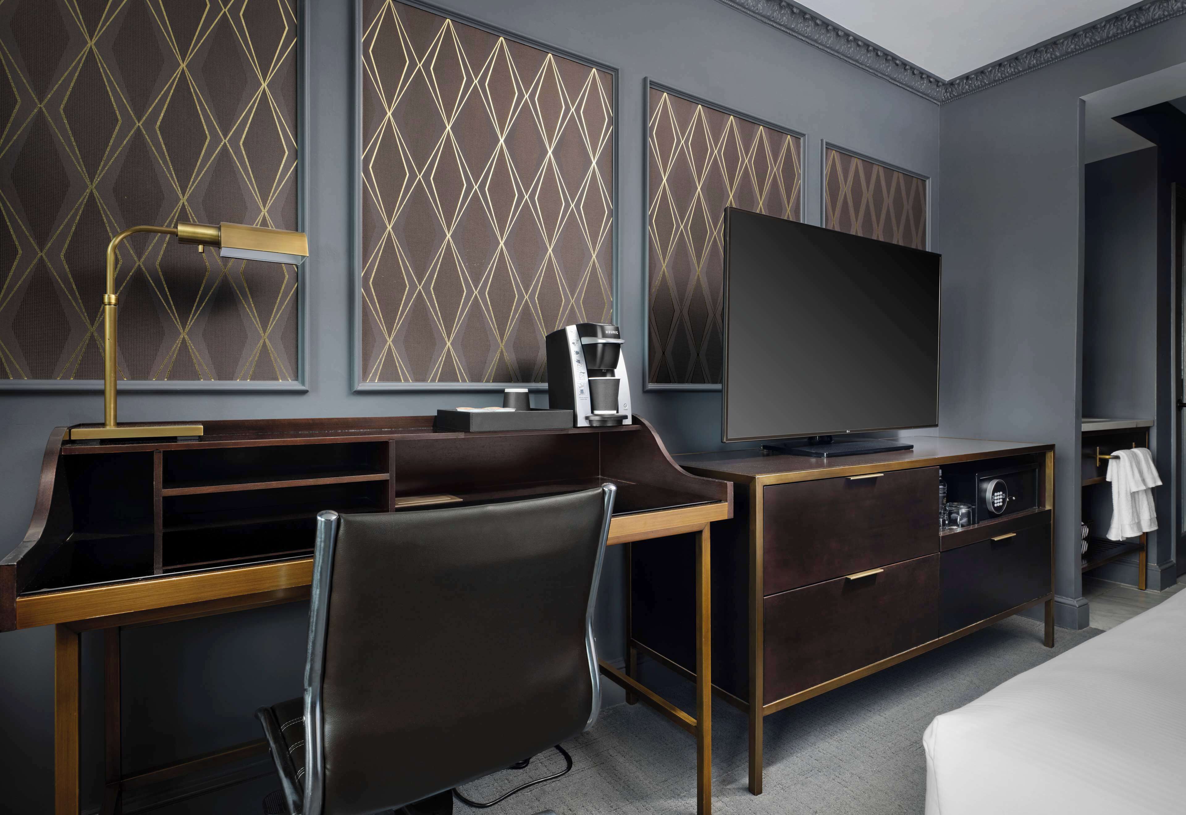 Ein modernes Hotelzimmer mit Schreibtisch, Stuhl, Fernseher und einer Minibar.