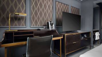 A modern hotel room with a desk, chair, television, and a minibar.
