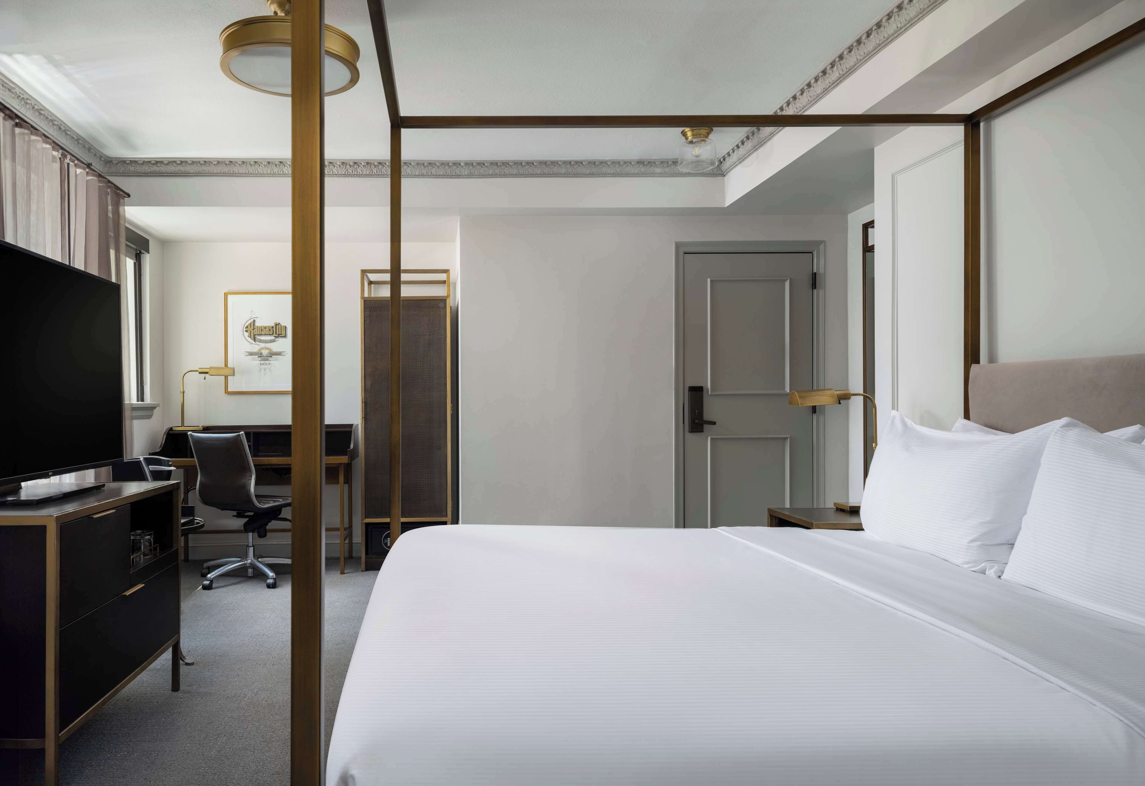 Habitación de hotel con una cama grande, un escritorio con silla, televisión y una puerta.