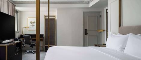 Habitación de hotel con una cama grande, un escritorio con silla, televisión y una puerta.