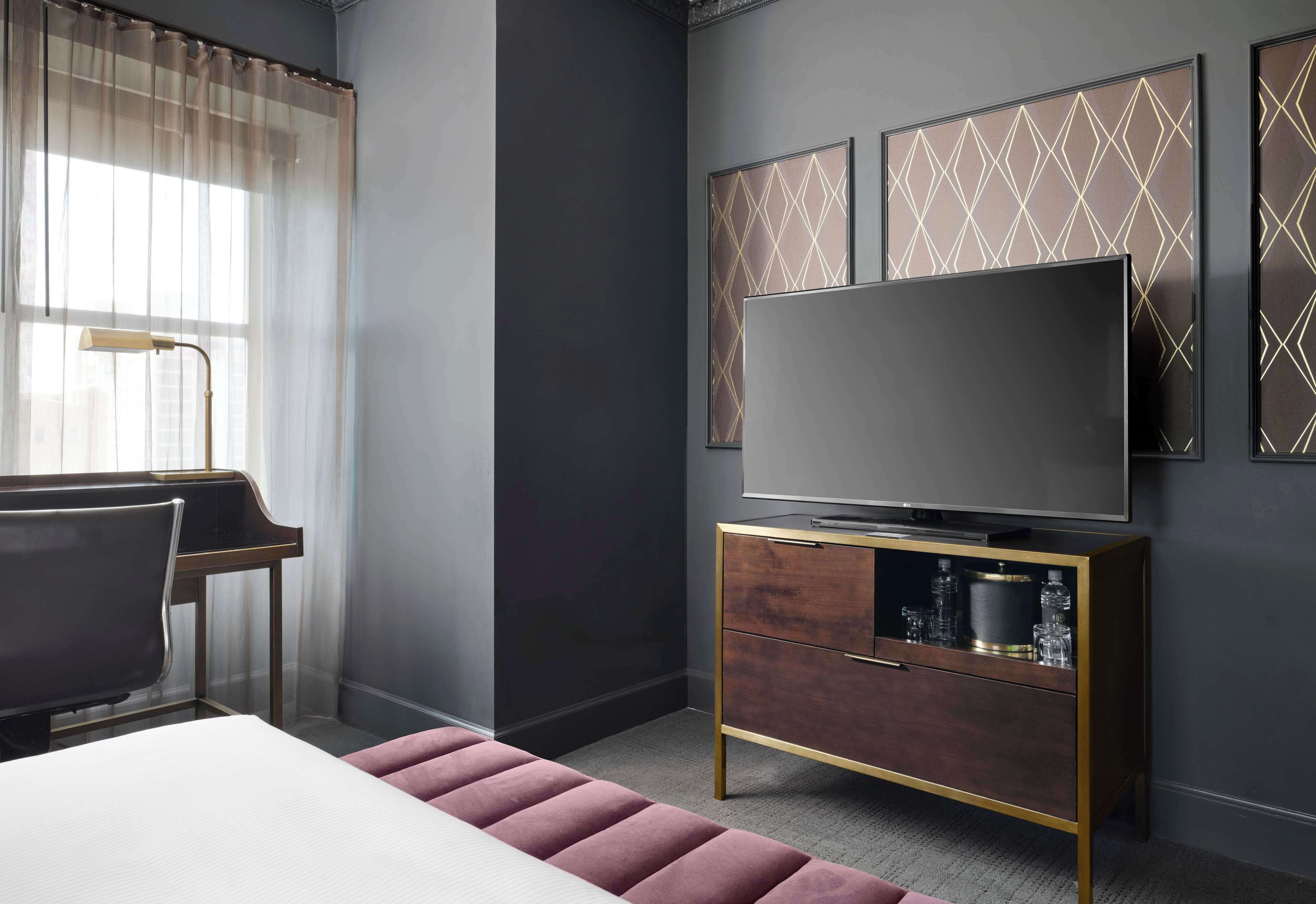 Et moderne hotelværelse med en stor seng, et skrivebord og et fjernsyn på et træskab.