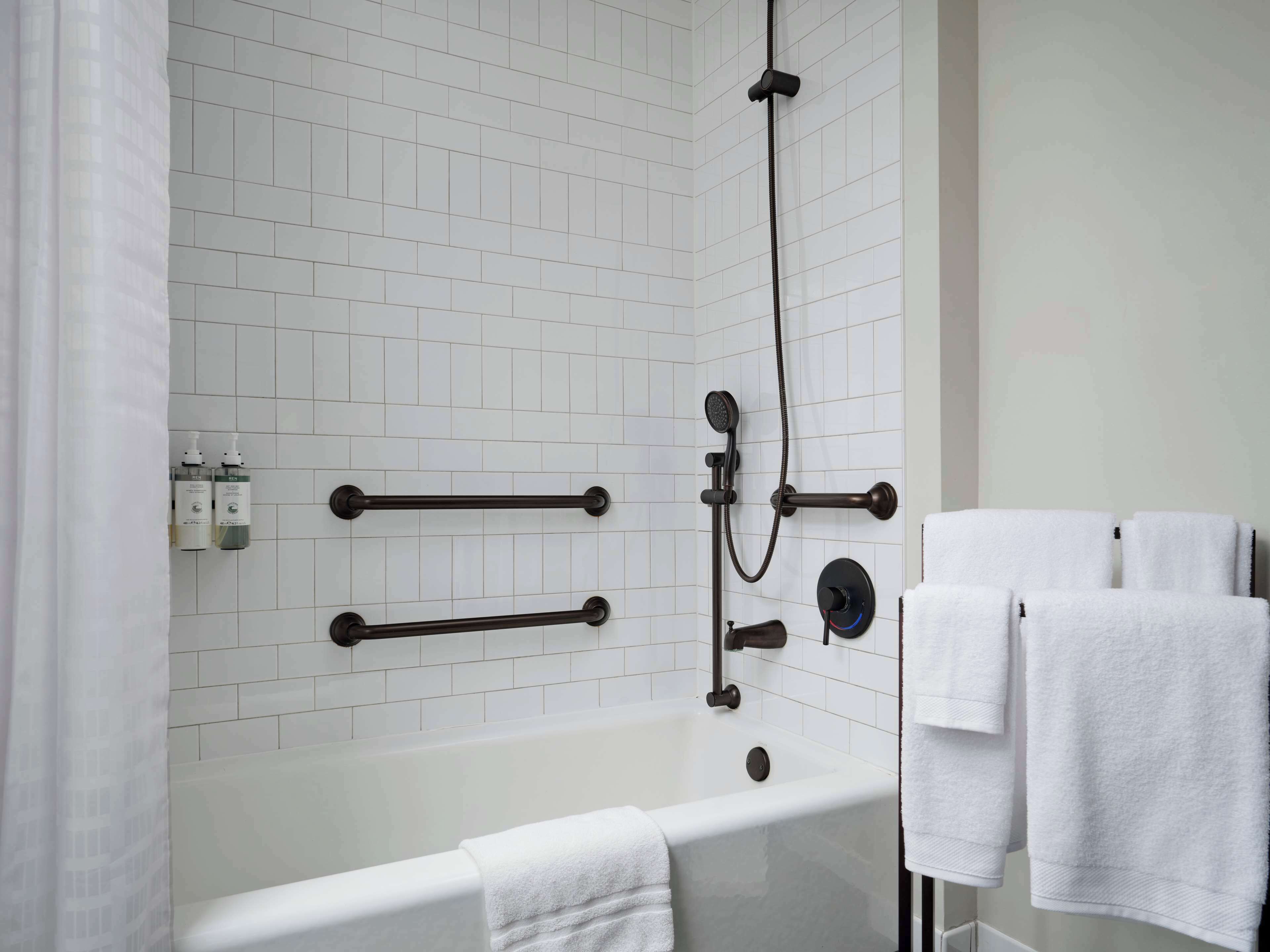 A bathroom with a white bathtub, a shower with a handheld showerhead, and two towel racks with white towels.