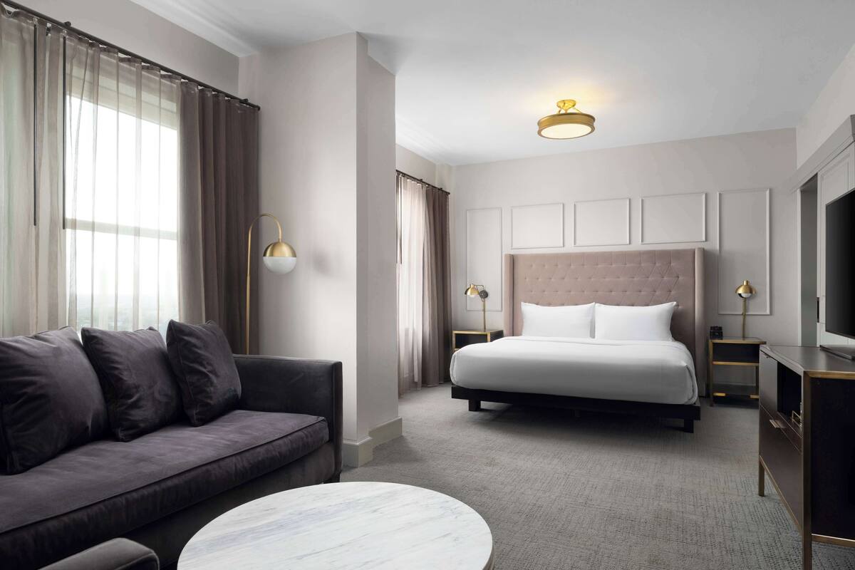 A hotel room with a bed, a sofa, a round coffee table, and a TV.