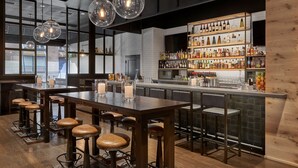 A bar area with wooden stools, a long bar counter, and a variety of bottles and glasses on shelves.