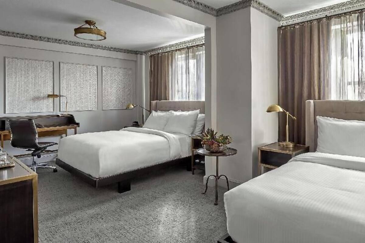 A hotel room with a large bed, a smaller bed, a desk, a chair, and a nightstand with a lamp.