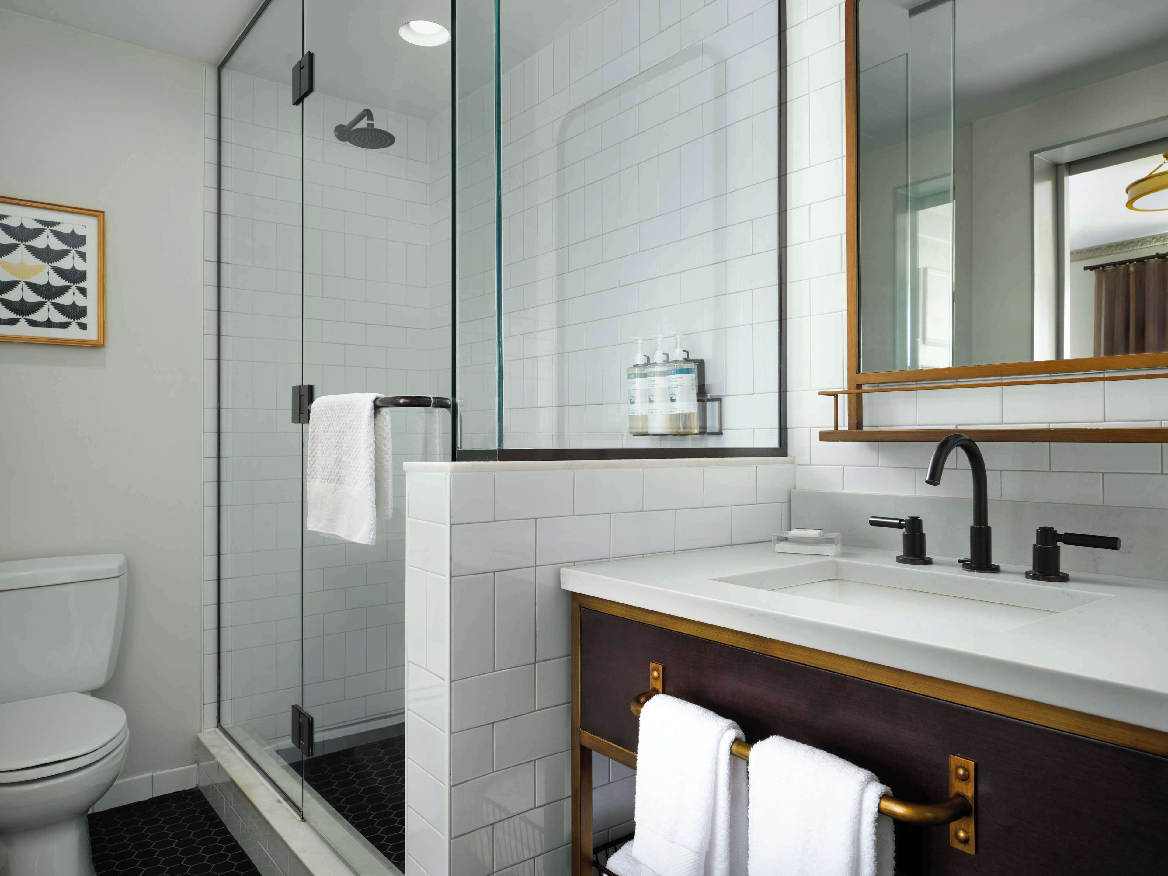 Un baño moderno con ducha envuelta en vidrio, un lavabo blanco sobre un mueble oscuro y un espejo grande.