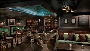 A dimly lit bar area with green upholstered seating, a bar counter, and framed pictures on the walls.