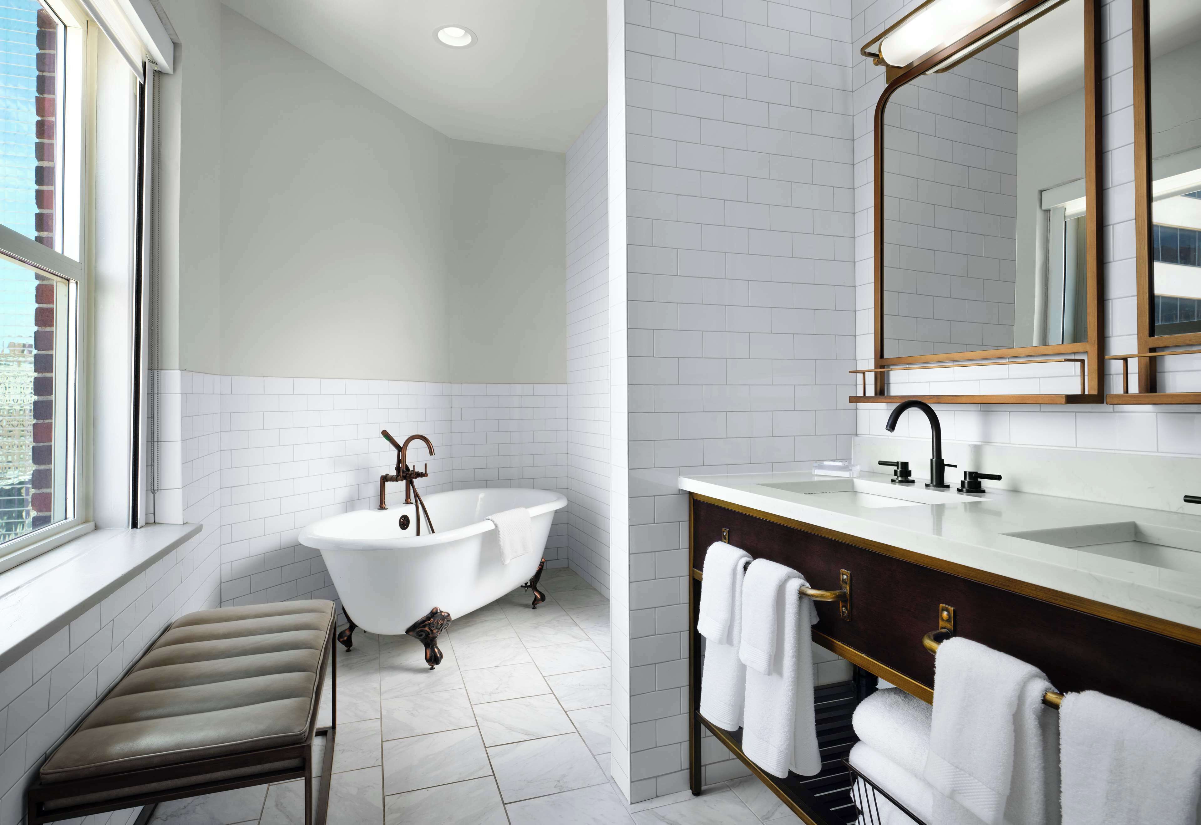 A modern bathroom with a freestanding bathtub, a vanity with a mirror, and a bench.