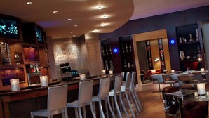 Een moderne bar met een lange toonbank, witte barkrukken en een combinatie van bar- en eettafels.