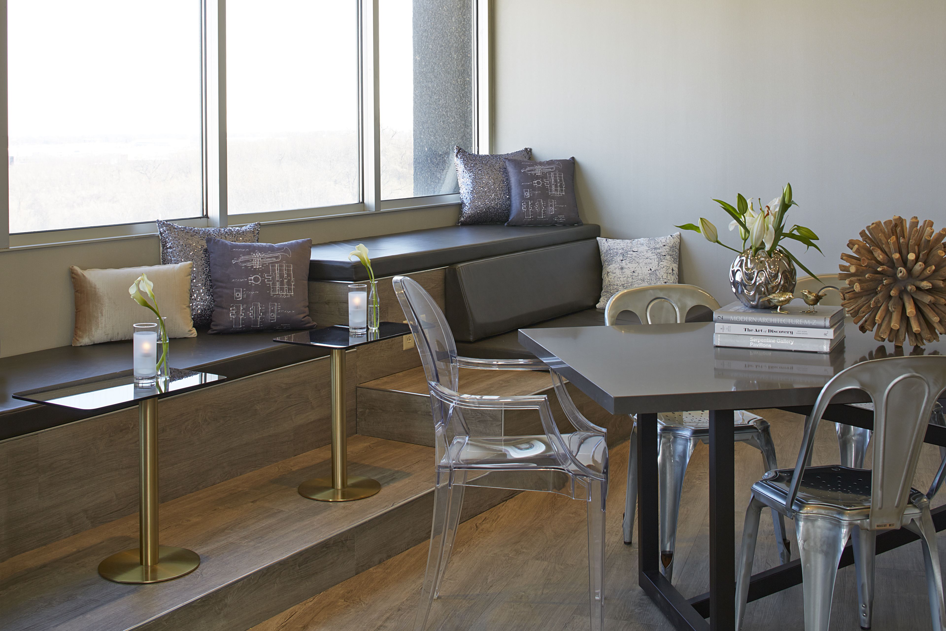A modern interior with a clear glass dining table, a bench with cushions, and a view of the outdoors through large windows.
