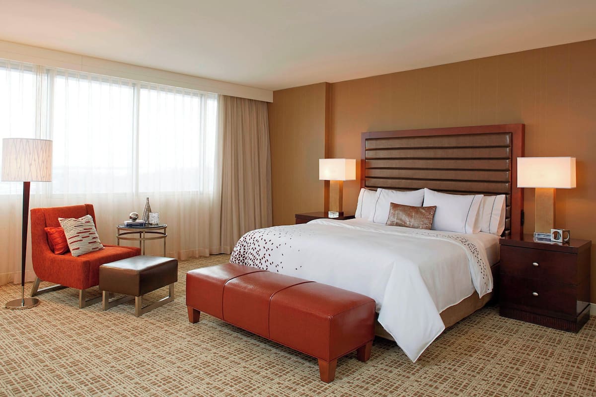 Ein Hotelzimmer mit einem großen Bett, einem roten Sessel, einem kleinen Tisch und einem Nachttisch mit Lampen.