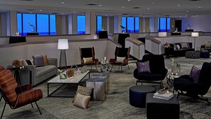 Een ruime hotellobby met diverse zithoeken, een receptiebalie en grote ramen met uitzicht op de stad.