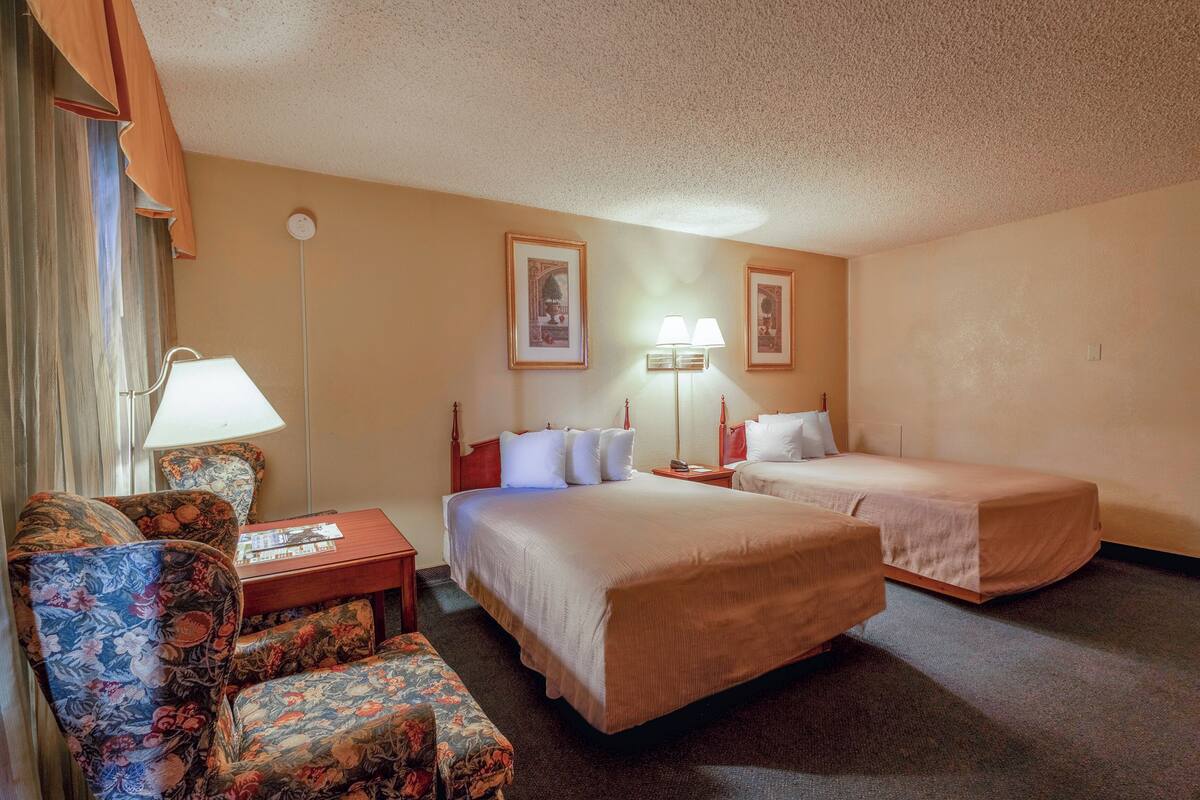 A hotel room with two beds, a sofa, a table, and two lamps.