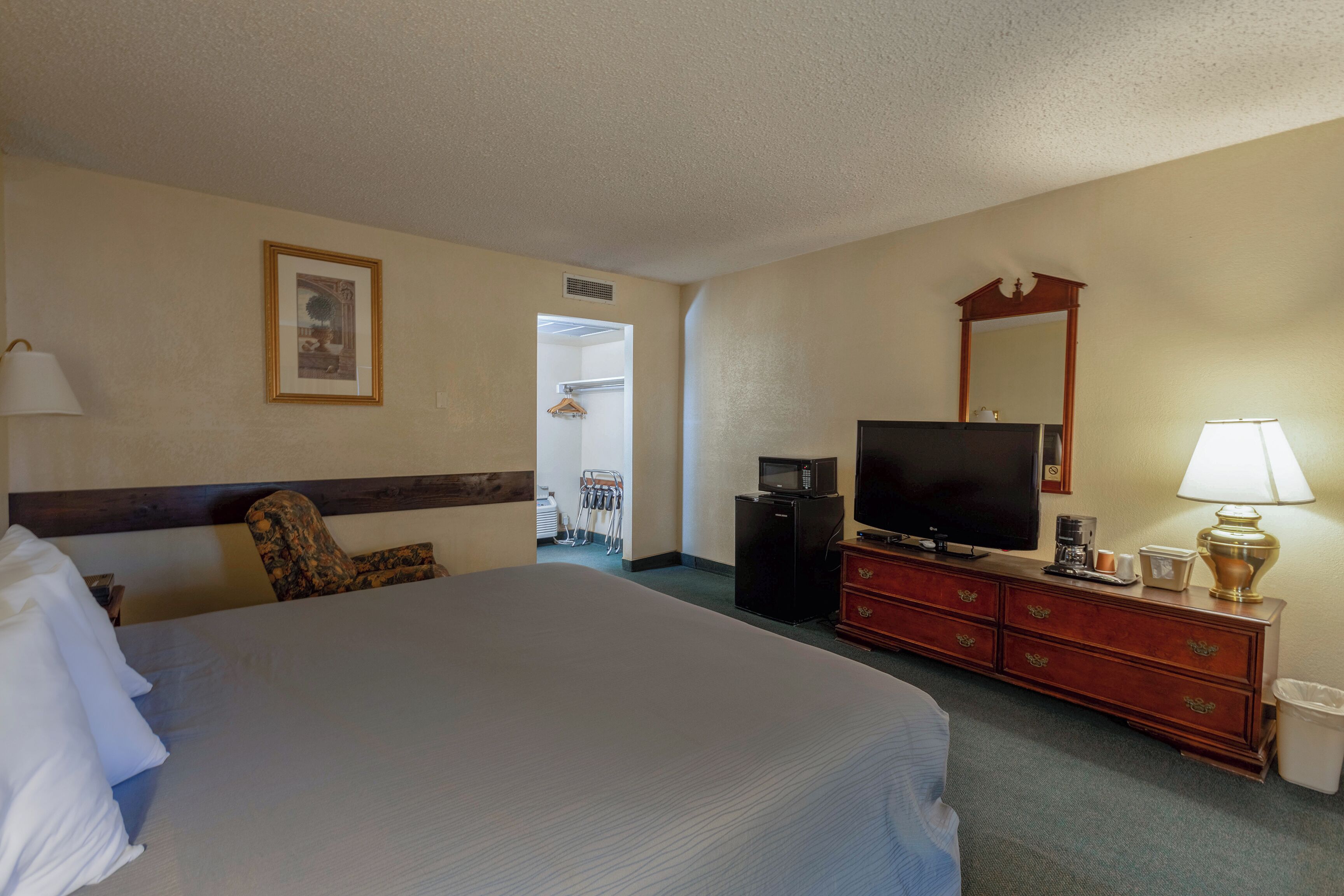 Una habitación de hotel con una cama grande, televisión, cómoda y espejo.
