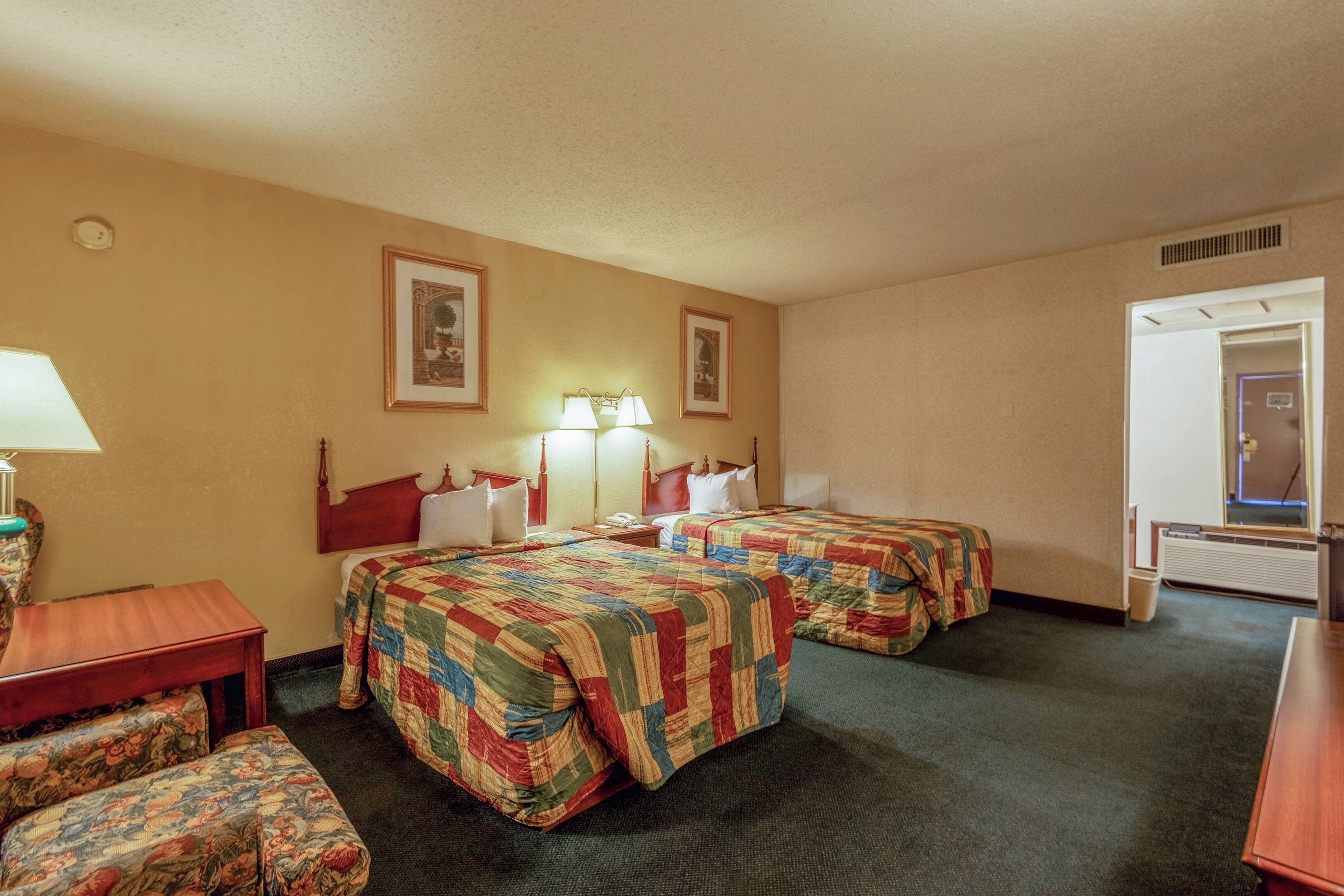 Habitación de hotel con dos camas, un escritorio, una silla, una lámpara y un cuadro en la pared.
