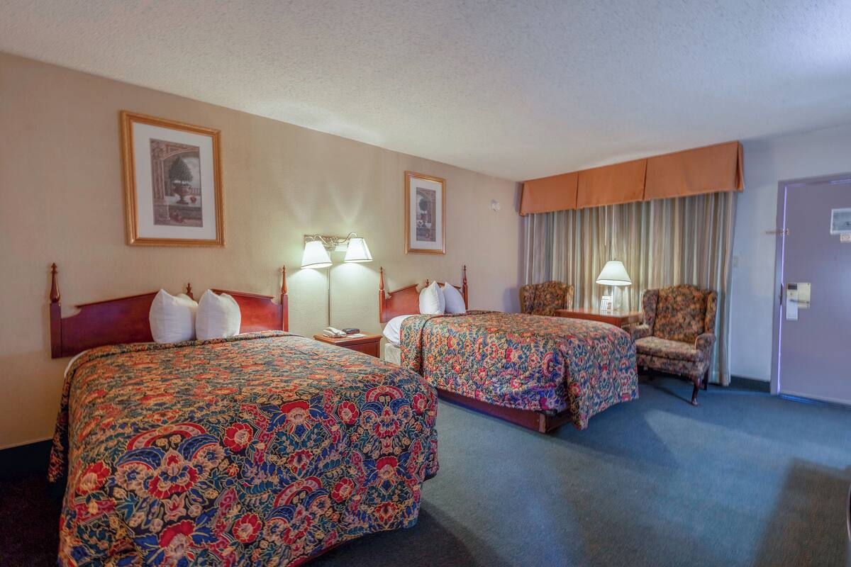 A hotel room with two beds, a chair, a lamp, and a door.