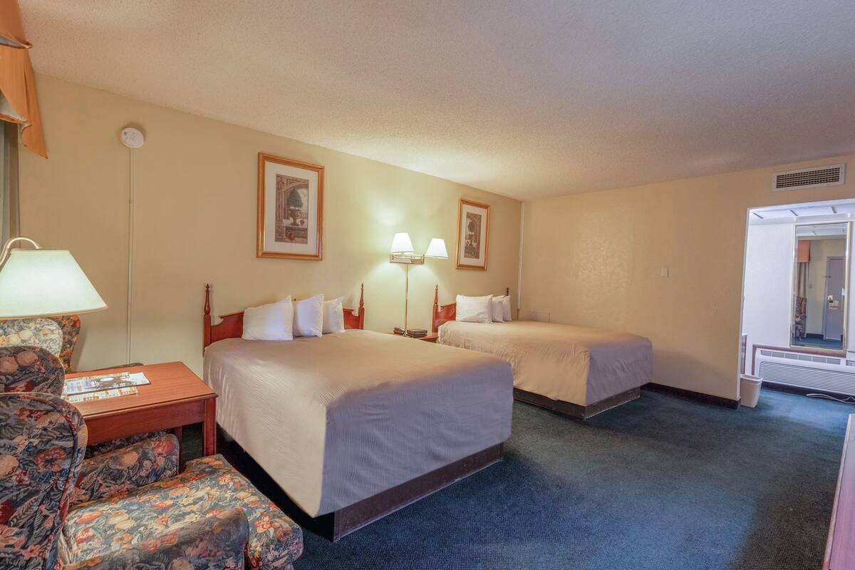 A hotel room with two beds, a desk with a lamp, a chair, and framed pictures on the wall.