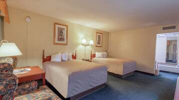 A hotel room with two beds, a desk with a lamp, a chair, and framed pictures on the wall.