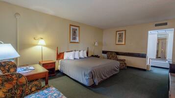 A hotel room with a bed, two chairs, a nightstand, a lamp, and a framed picture on the wall.