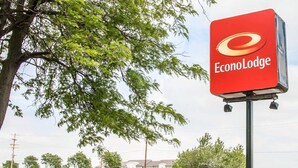 Une enseigne pour l’EconLodge, offrant une vue dégagée sur les environs aménagés, notamment les arbustes et un bâtiment situé au loin.