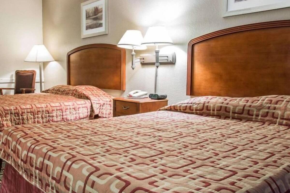 A hotel room with two beds, a nightstand, a lamp, and a framed picture on the wall.