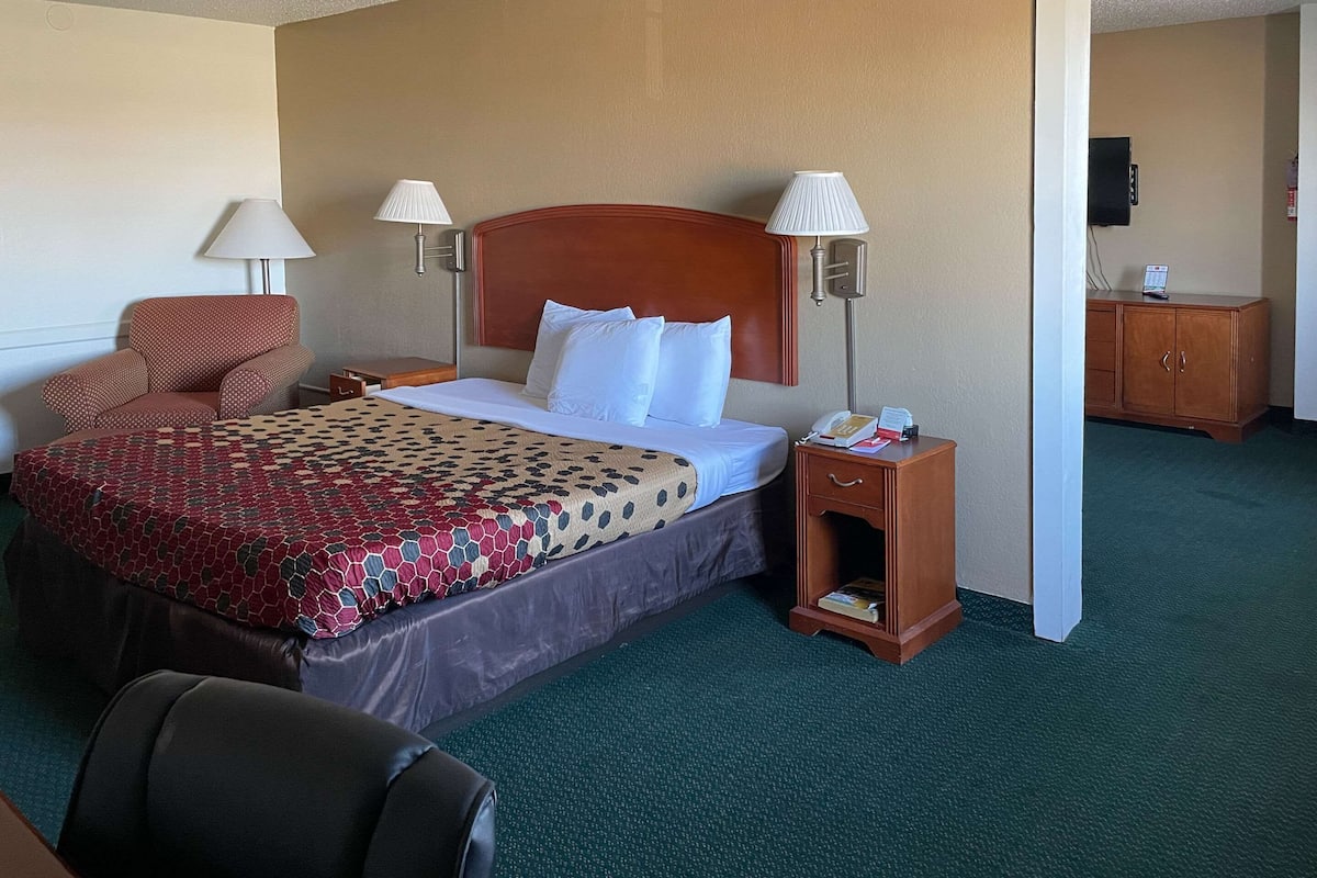 A hotel room with a large bed, two bedside lamps, a wooden nightstand, a chair, and a television on a cabinet.