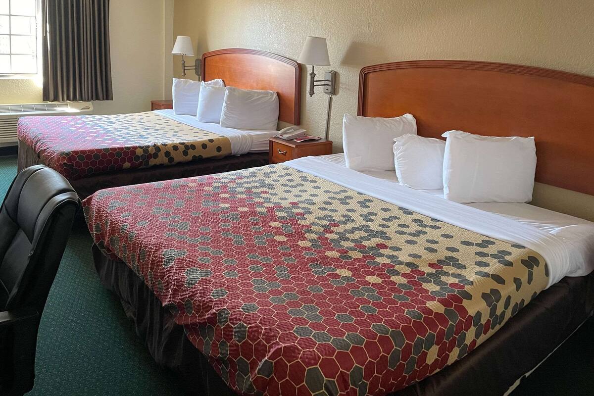 Two double beds with patterned bedspreads, bedside lamps, a nightstand with a phone, and a chair.
