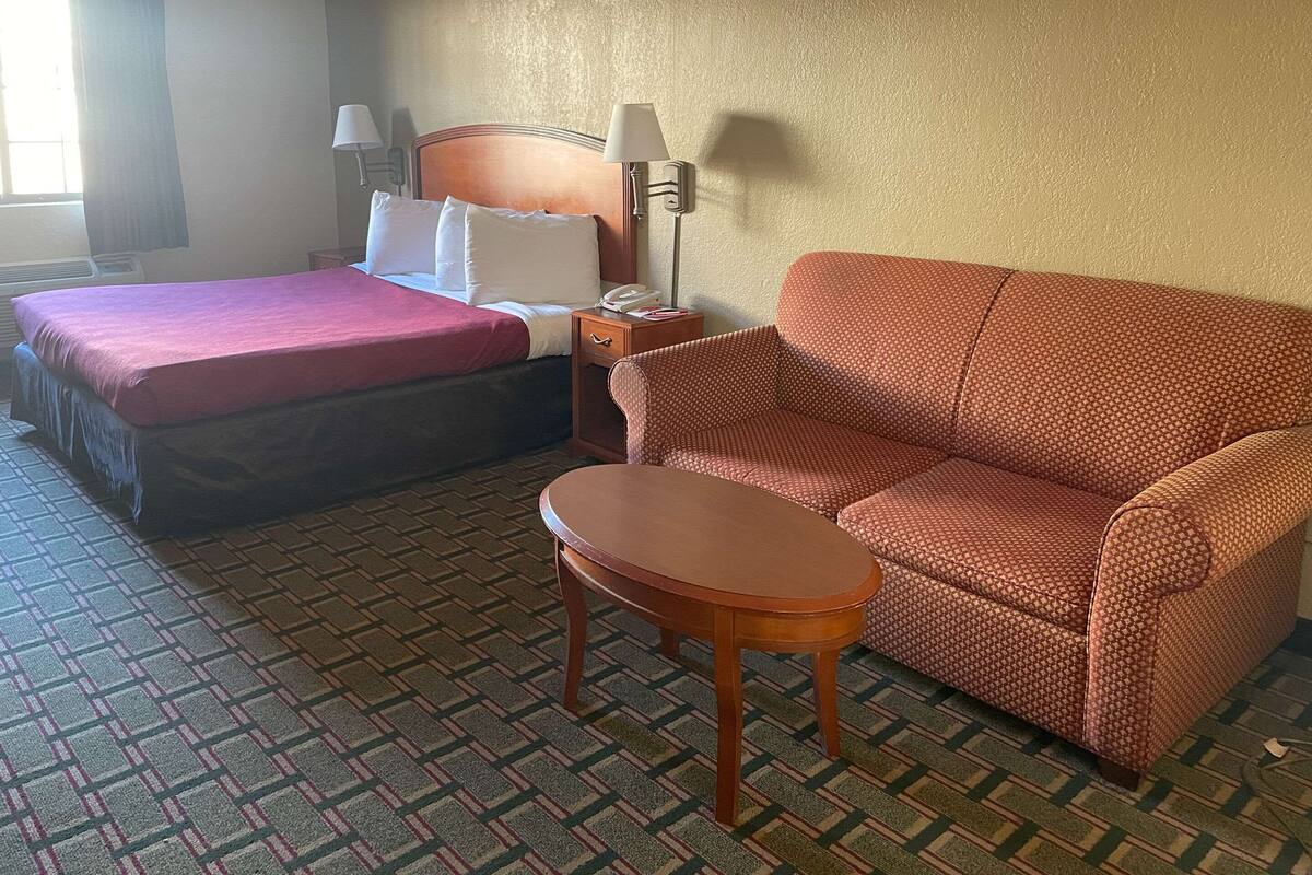 A hotel room with a bed, a sofa, a small table, and a lamp.