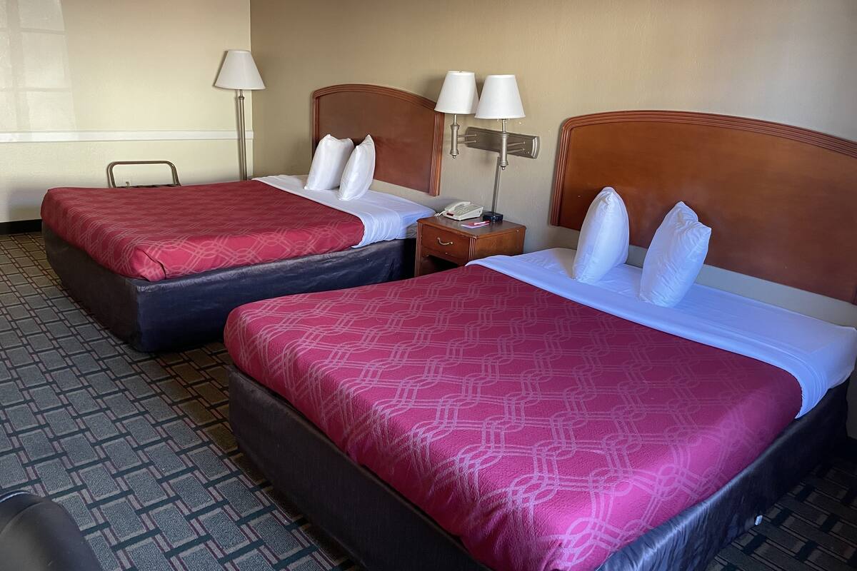 A hotel room with two beds, each with a red patterned bedspread, white pillows, and a wooden headboard. There are two bedside tables with lamps and a telephone.