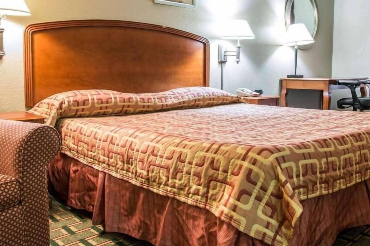 A hotel room with a bed, a desk, a chair, and a mirror.
