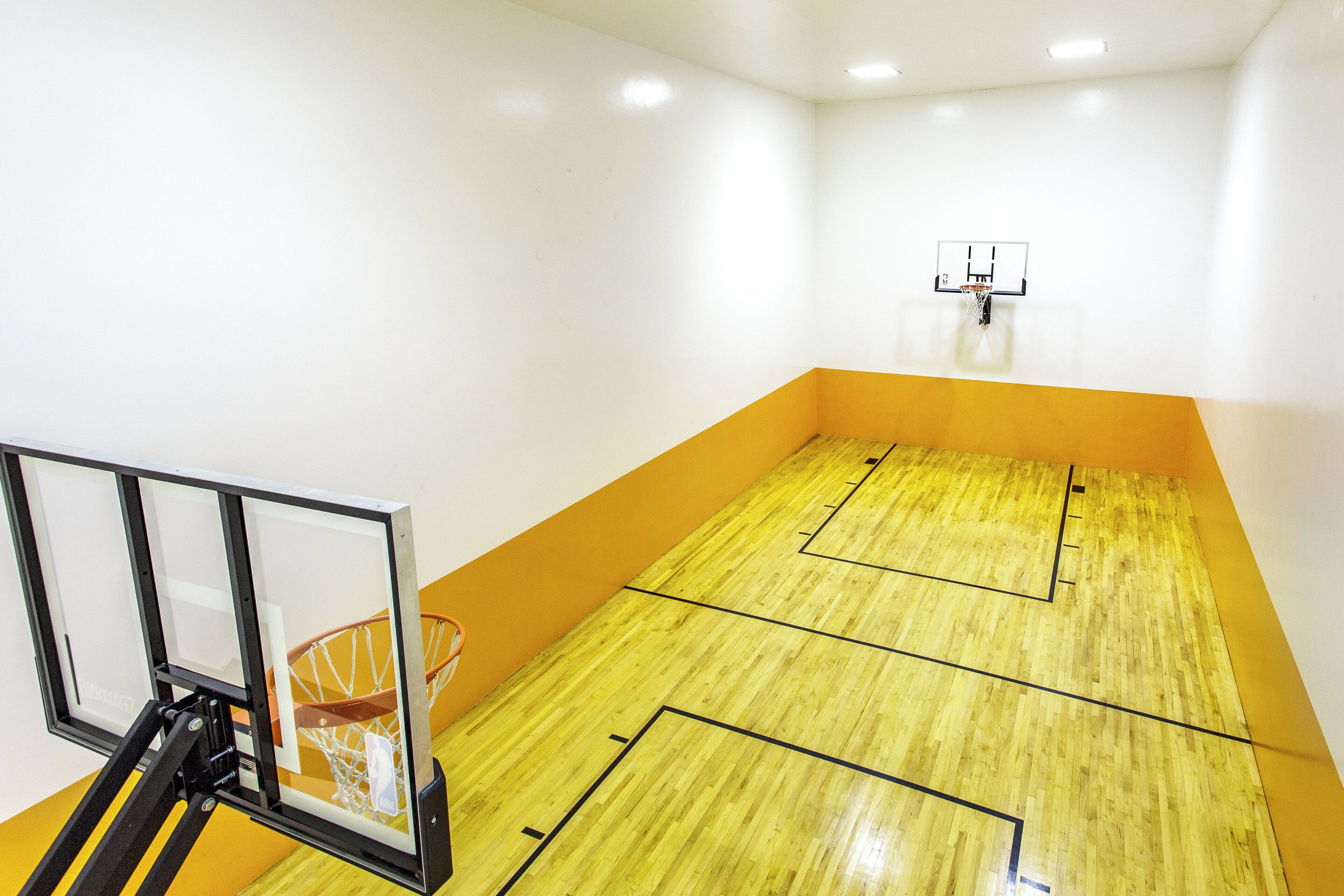 Una cancha de baloncesto con aro y tablero, piso de madera y borde amarillo.