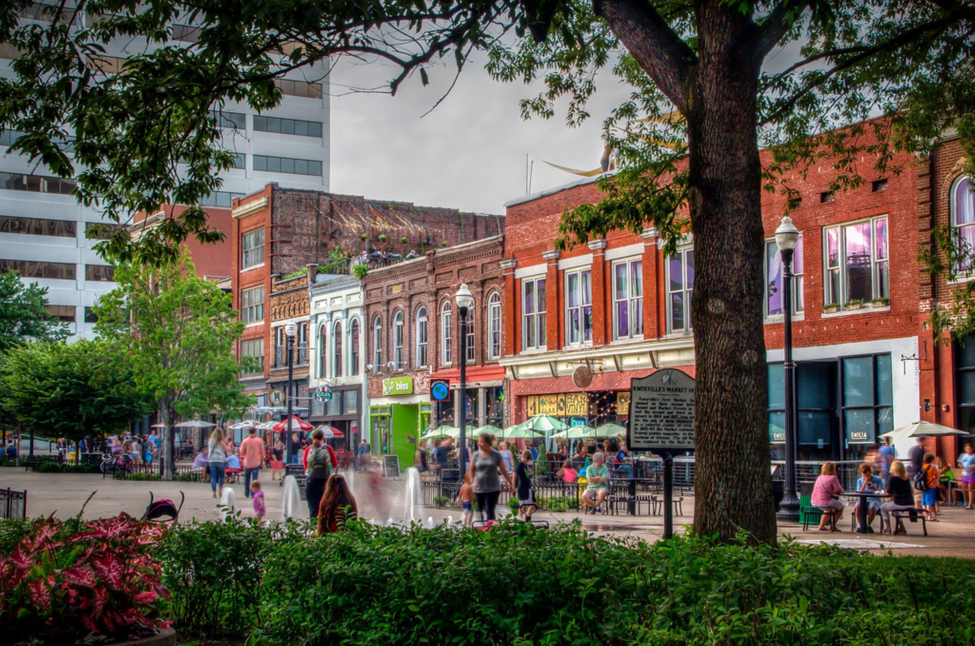 A public square with historic buildings, outdoor seating, and a fountain.