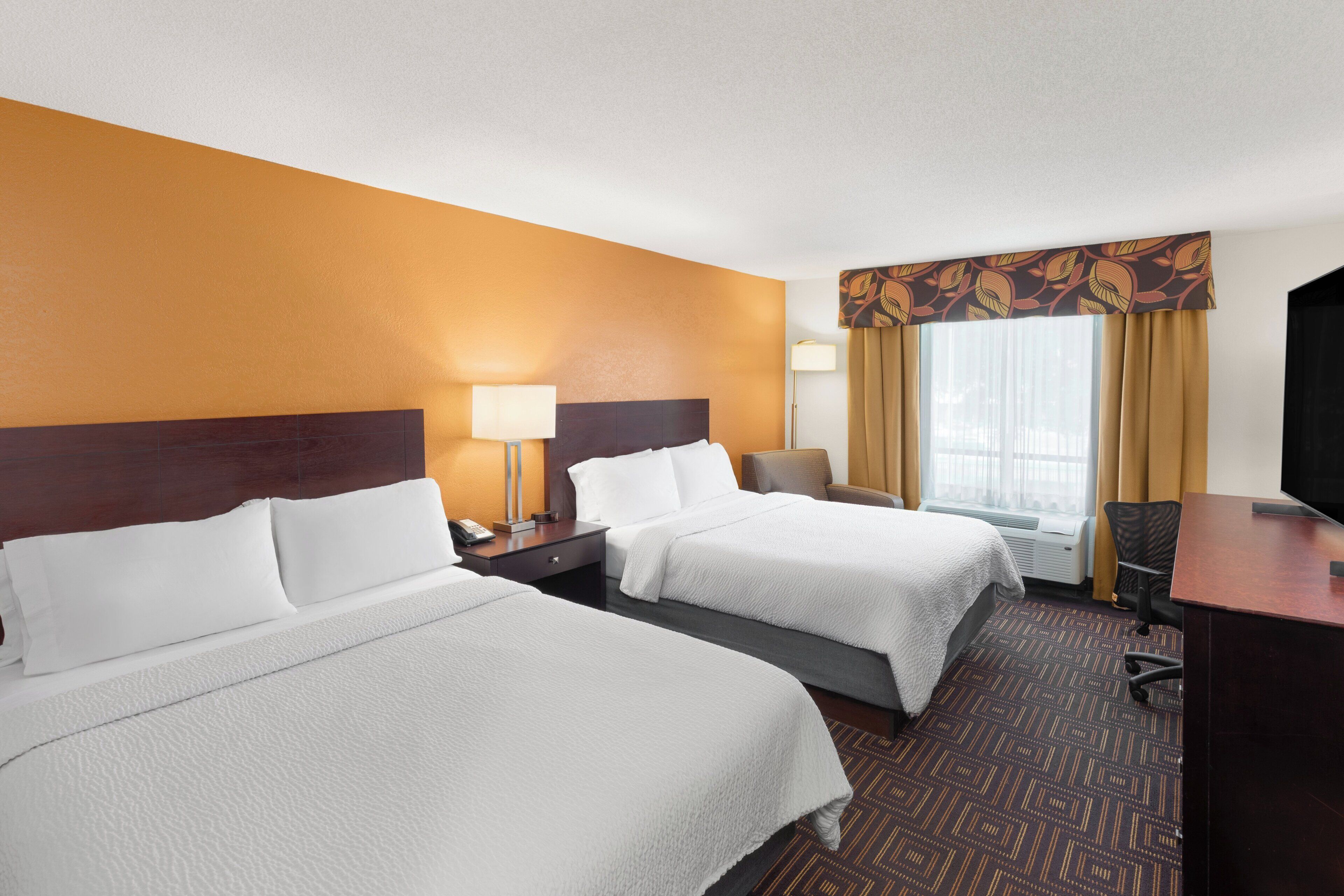 A hotel room with two beds, a desk, a chair, and a television.