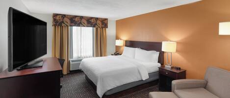 A hotel room with a bed, bedside tables, a desk, a TV, and a sofa.