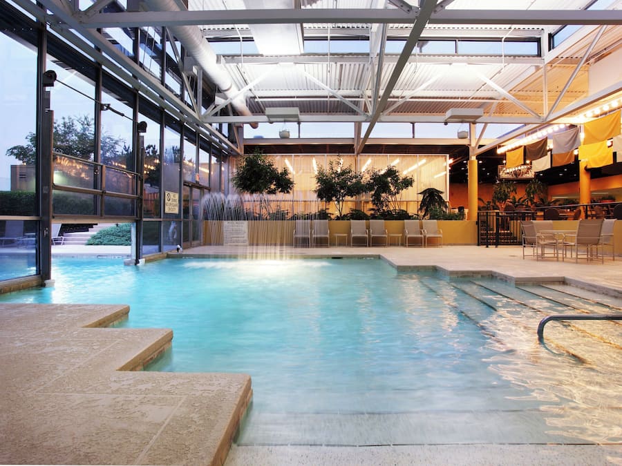 Une piscine intérieure agrémentée d’une cascade, entourée d’espaces aménagés pour s’asseoir et de plantes en pot.
