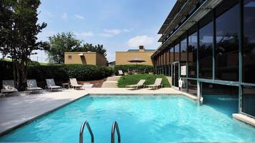 A swimming pool with lounge chairs and a no diving sign, surrounded by a building with large windows.