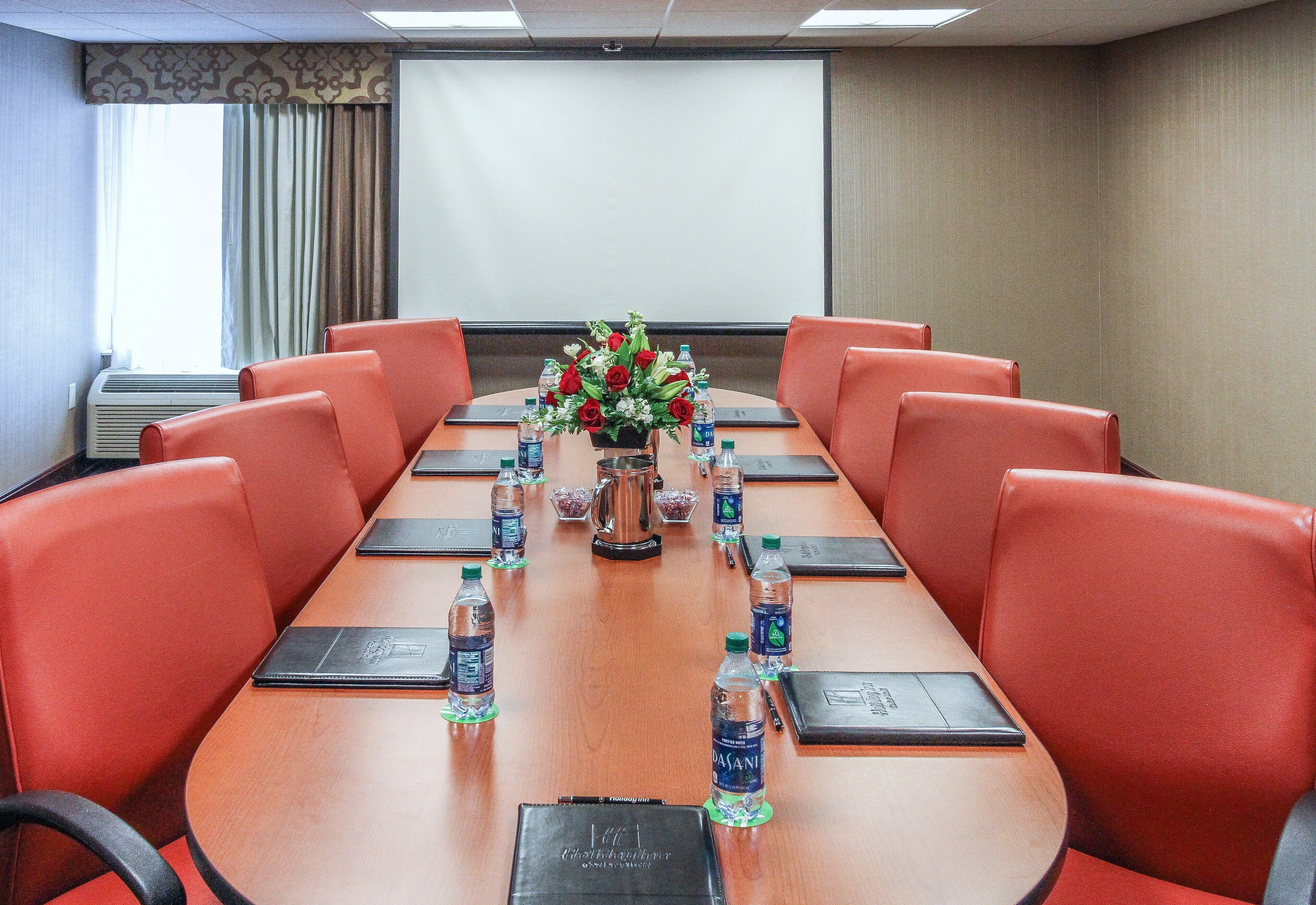 A conference room with a long table, red chairs, water bottles, and a flower arrangement.