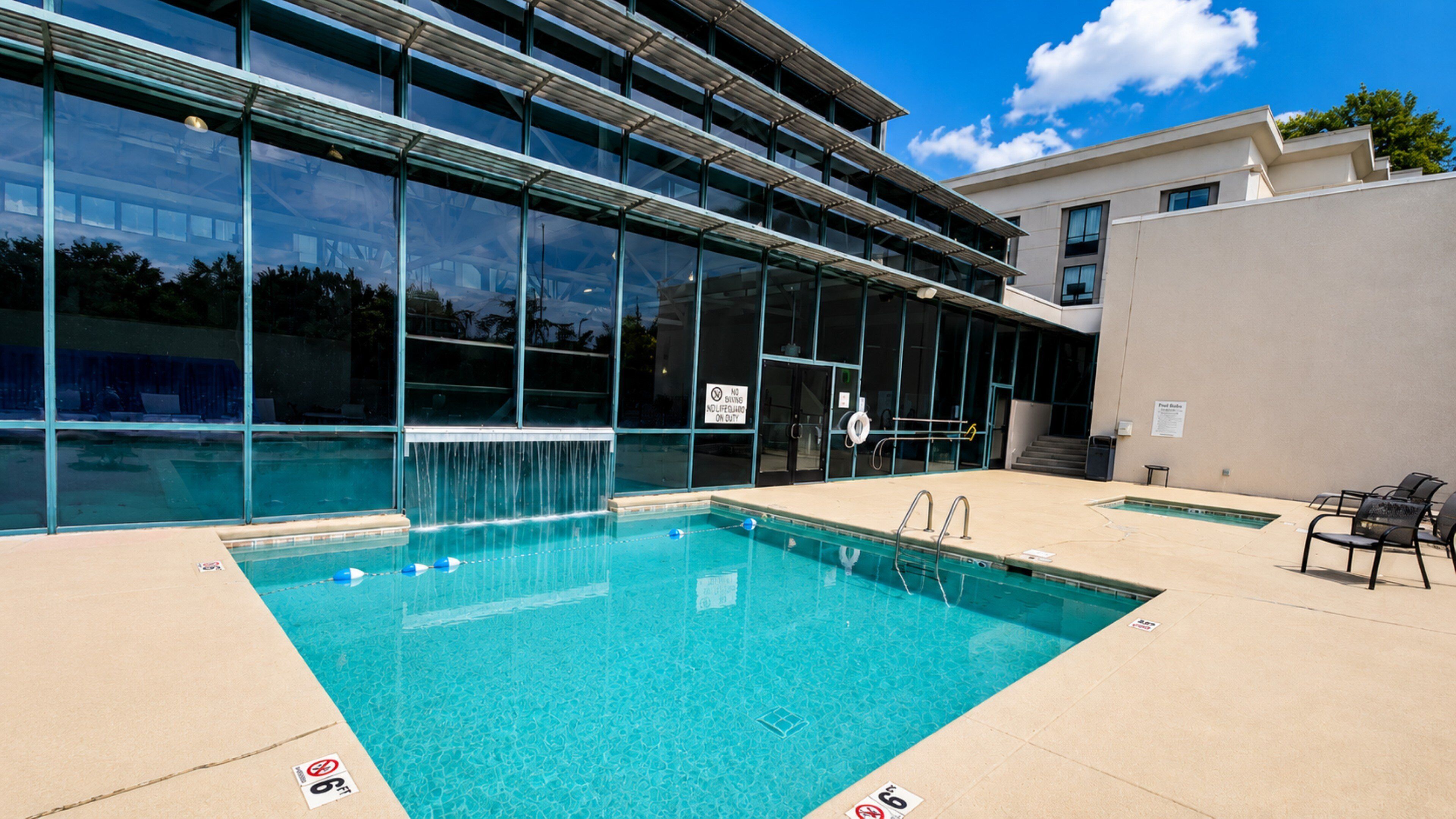 Une piscine à l’eau d’un bleu cristallin, entourée d’un bâtiment moderne doté de grandes fenêtres et d’un poste de surveillance pour les sauveteurs.