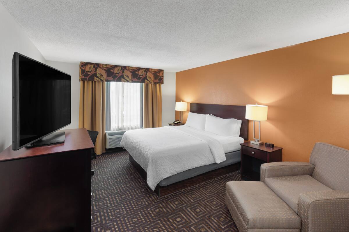 A hotel room with a bed, a TV, a desk, a chair, and a lamp.