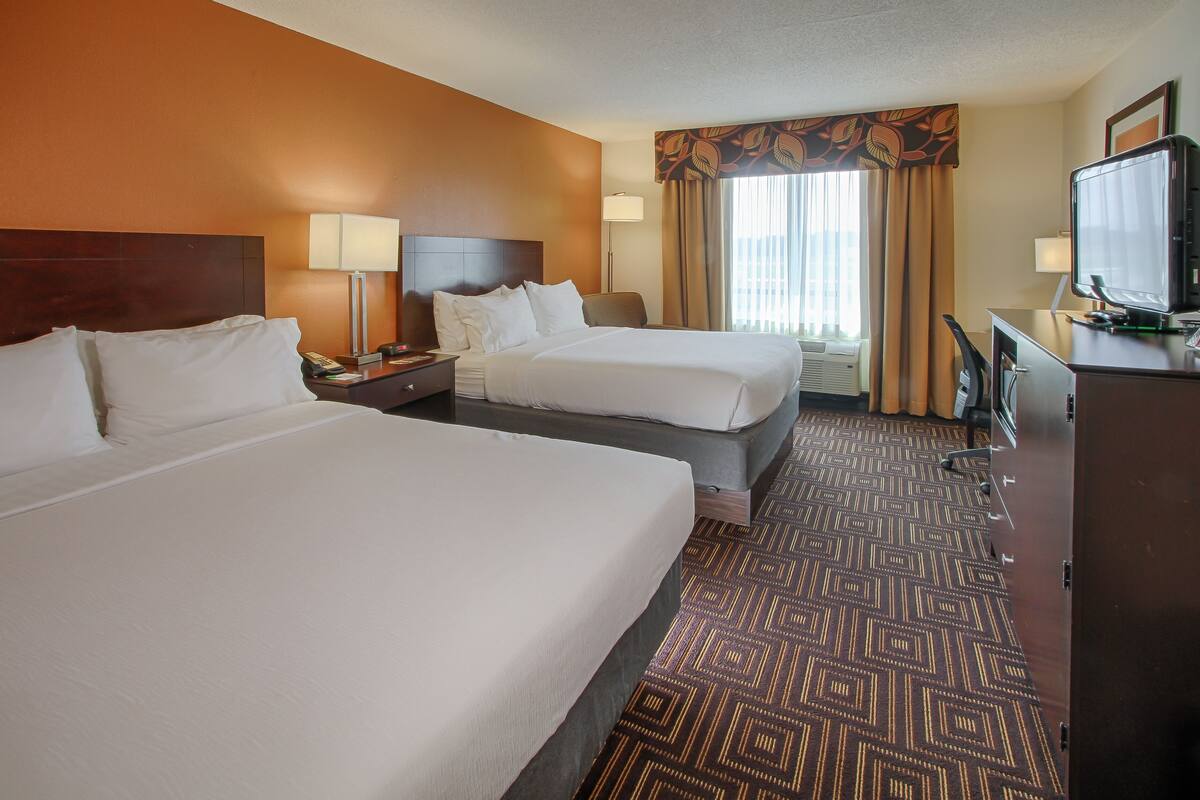 A hotel room with two beds, a desk with a television, and a patterned carpet.