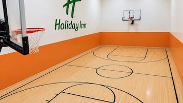 Una cancha de baloncesto con dos aros de baloncesto, el logotipo de Holiday Inn en la pared y detalles en color naranja.