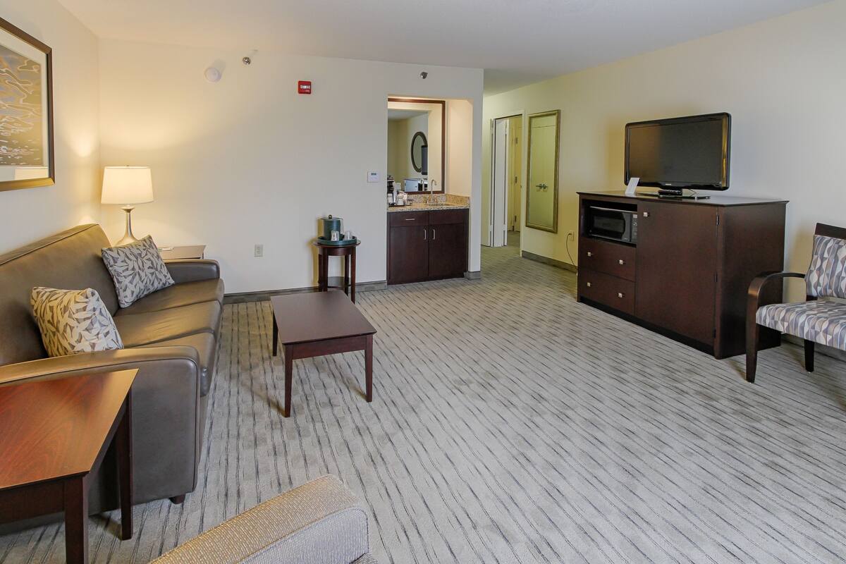 A hotel room with a sofa, a coffee table, a TV, a microwave, and a small kitchenette.