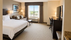 Una habitación de hotel con cama, escritorio, silla, televisor y ventana con cortinas.