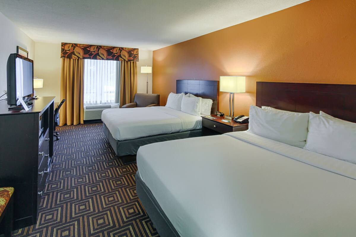 A hotel room with two beds, a desk with a computer, a chair, and a TV.