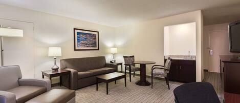 Una habitación de hotel con sofá, sillón, una pequeña mesa, una silla, televisión y un cuadro en la pared.