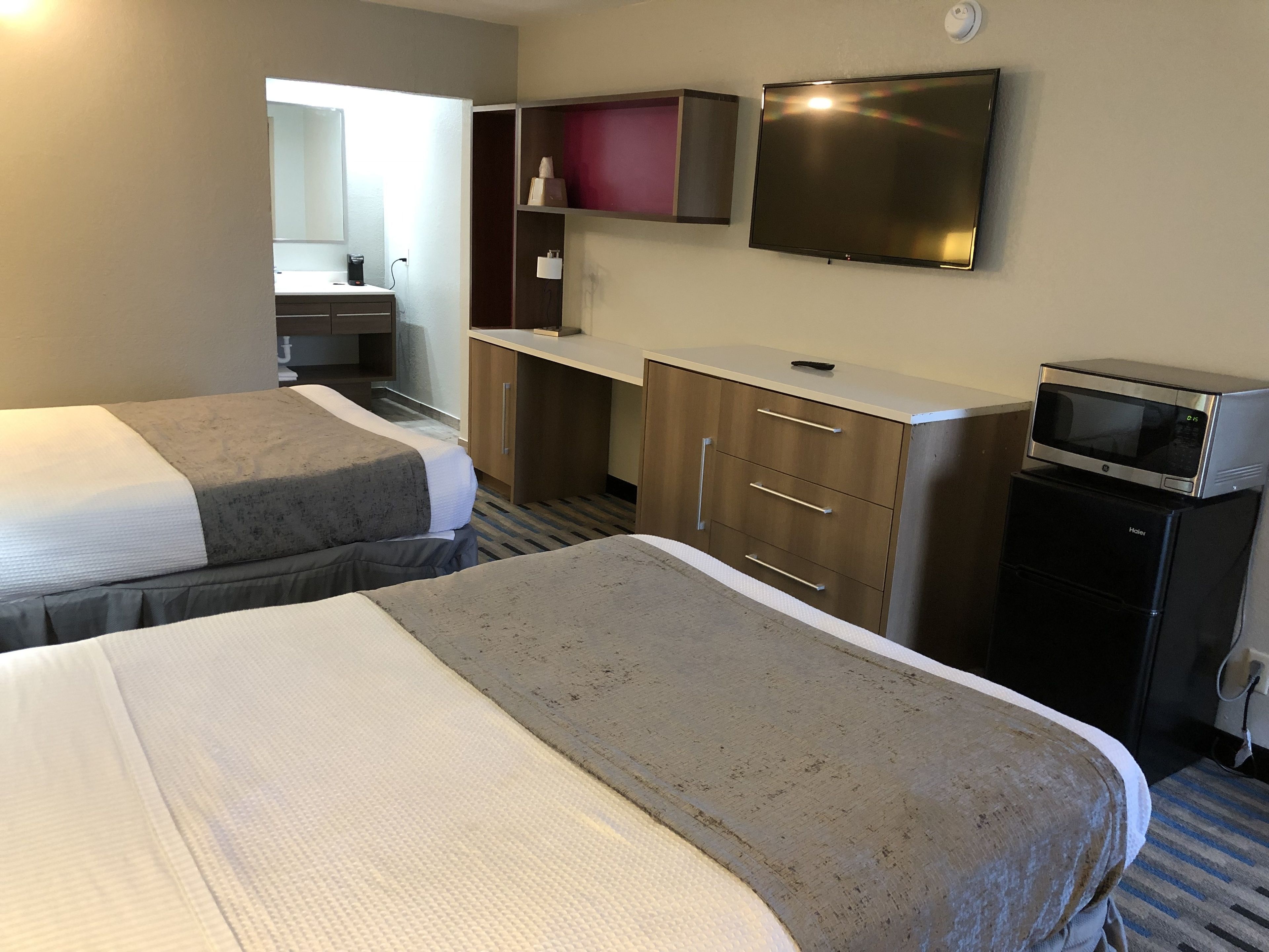 A hotel room with two beds, a desk, a microwave, and a television.