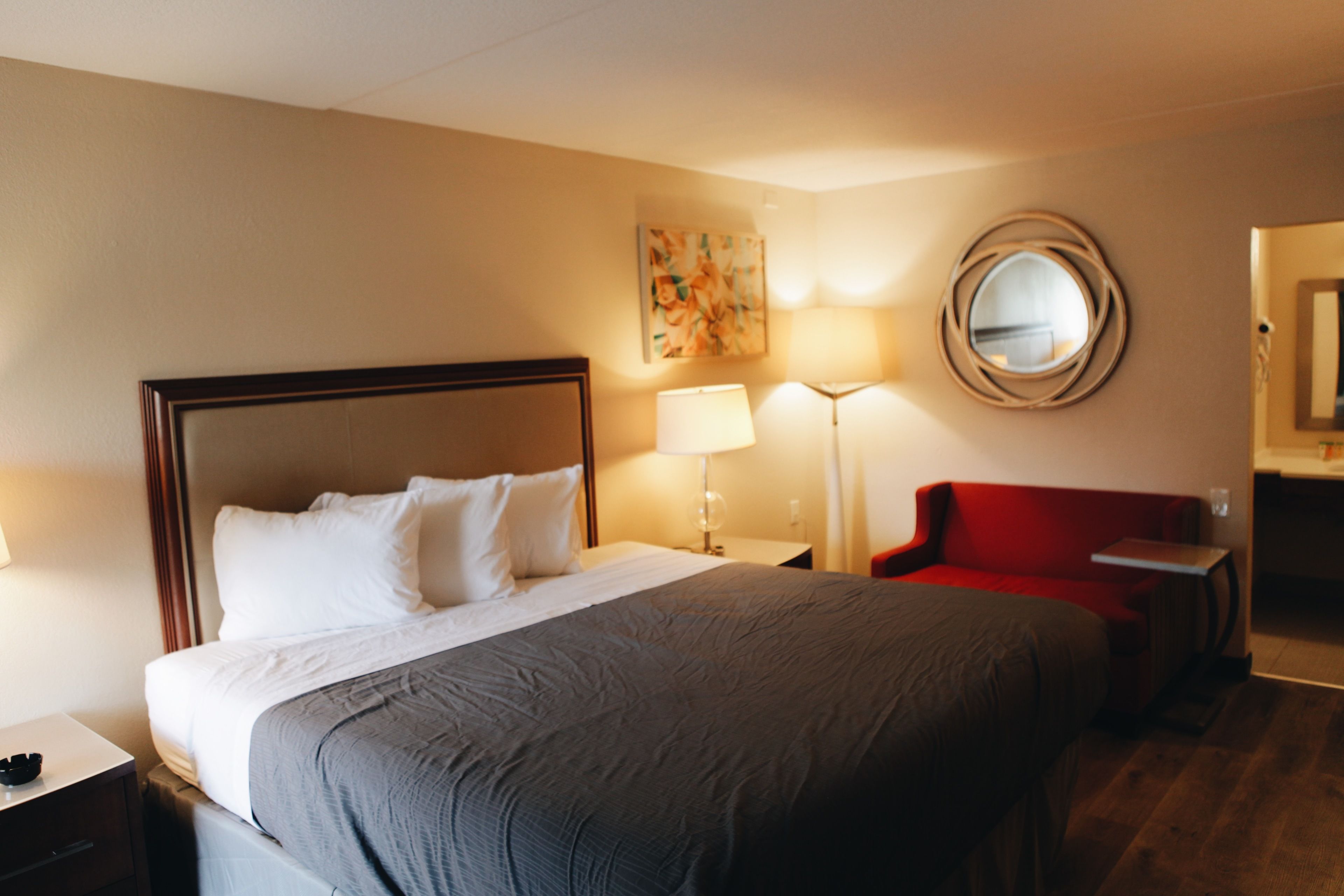 Una habitación de hotel con una cama grande, un sillón rojo, un escritorio y un espejo en la pared.